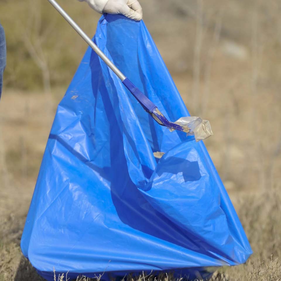Volunteers in purple shirts carrying large bags of collected desert waste